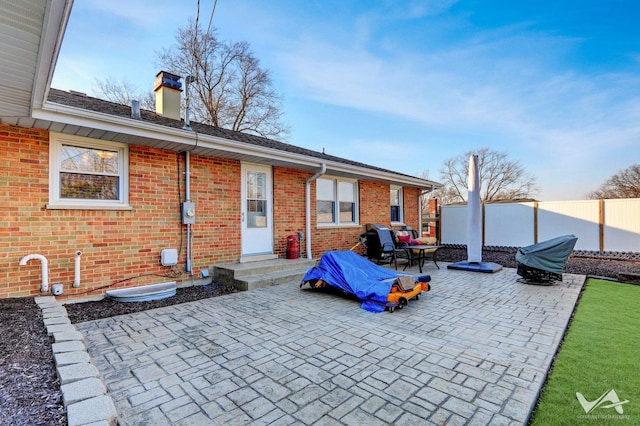 rear view of property featuring brick siding, a chimney, fence, and a patio