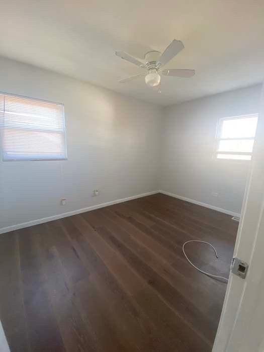 spare room with dark wood finished floors, baseboards, and ceiling fan