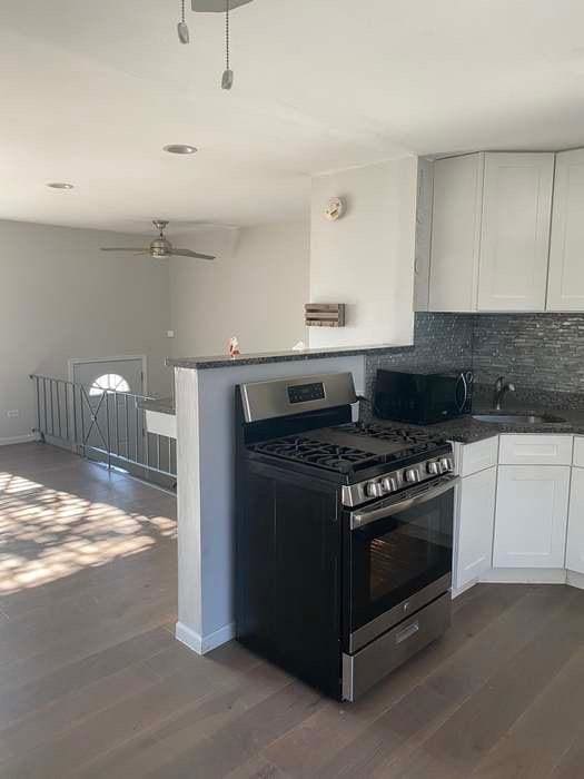 kitchen featuring white cabinets, appliances with stainless steel finishes, backsplash, dark wood-style flooring, and a sink