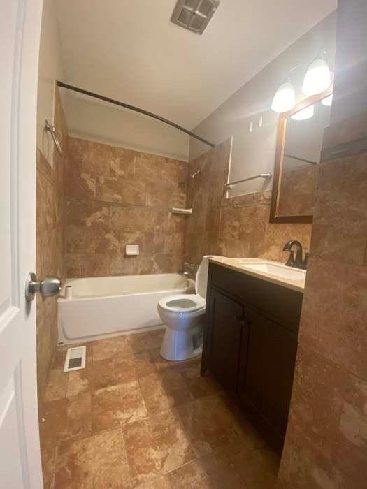 bathroom with visible vents, tile walls, toilet, and tub / shower combination