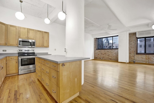 kitchen with stainless steel appliances, hanging light fixtures, light wood-style floors, open floor plan, and brick wall