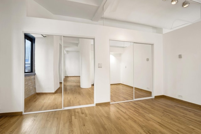 unfurnished bedroom featuring wood finished floors, beamed ceiling, two closets, and baseboards