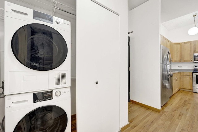 laundry area featuring stacked washer / dryer, laundry area, baseboards, and light wood finished floors