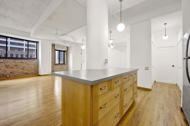 kitchen featuring beam ceiling, hanging light fixtures, light wood-style flooring, and brick wall