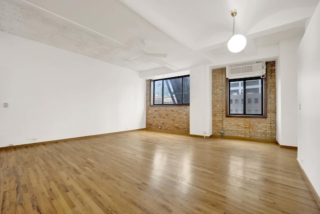 empty room with brick wall, baseboards, wood finished floors, and a wall mounted air conditioner