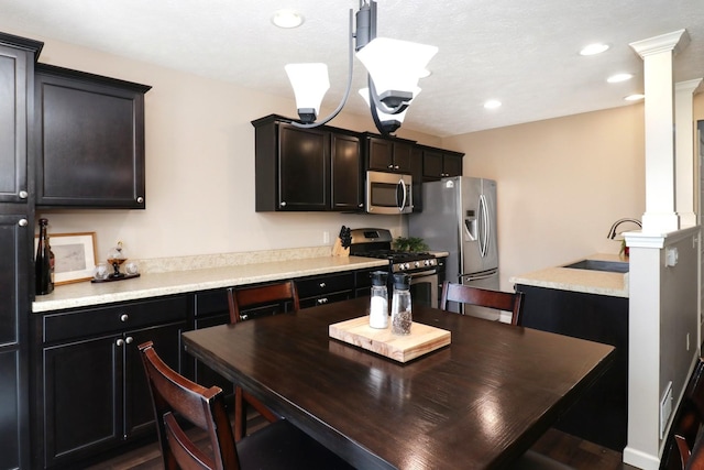 kitchen featuring appliances with stainless steel finishes, an inviting chandelier, light countertops, ornate columns, and a sink