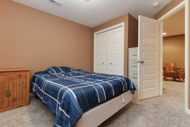 bedroom featuring a closet, visible vents, light carpet, and a textured ceiling