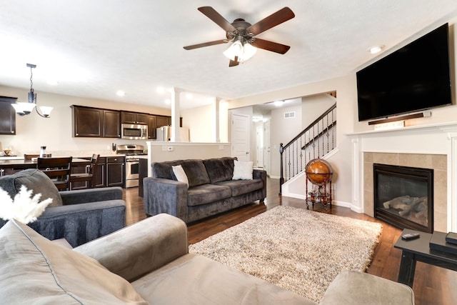 living area with dark wood-type flooring, a tile fireplace, baseboards, and stairs