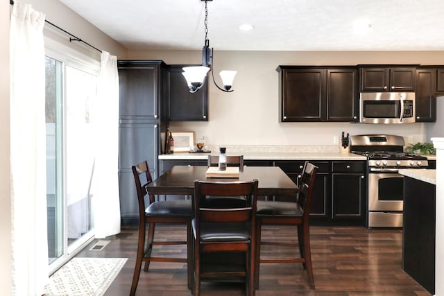 kitchen with dark wood-style flooring, decorative light fixtures, stainless steel appliances, light countertops, and a notable chandelier