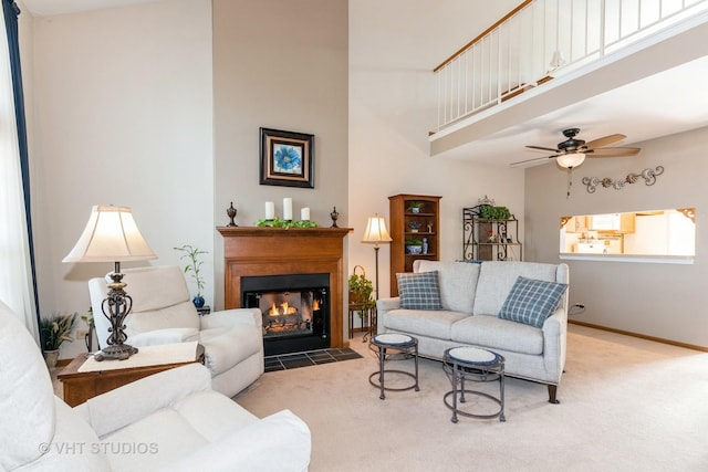 carpeted living area featuring baseboards, a fireplace with flush hearth, a high ceiling, and a ceiling fan