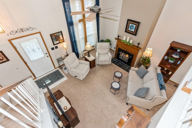 carpeted living room with a high ceiling, a fireplace with flush hearth, and ceiling fan