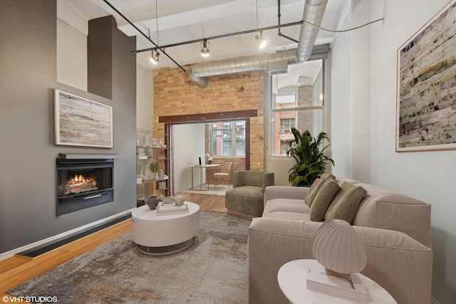 living room with a towering ceiling, a warm lit fireplace, wood finished floors, and rail lighting