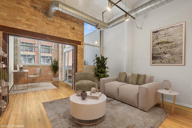 living room with brick wall, wood finished floors, a towering ceiling, and baseboards