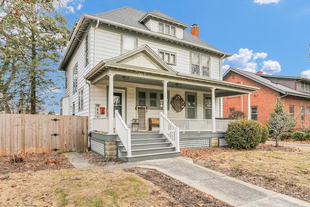 american foursquare style home with roof with shingles, a chimney, covered porch, a gate, and fence