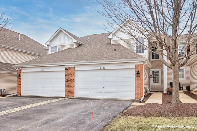 multi unit property with driveway, a shingled roof, and brick siding