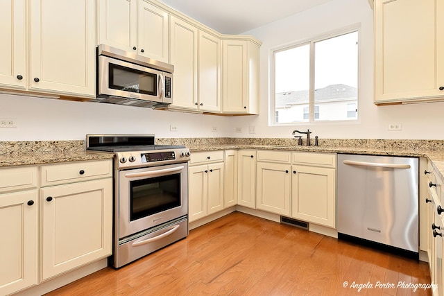 kitchen featuring visible vents, appliances with stainless steel finishes, light stone countertops, light wood-style floors, and a sink