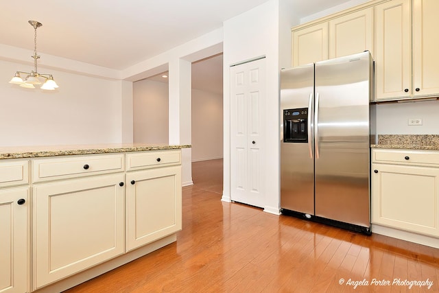 kitchen with cream cabinets, light wood-style floors, stainless steel fridge, and decorative light fixtures