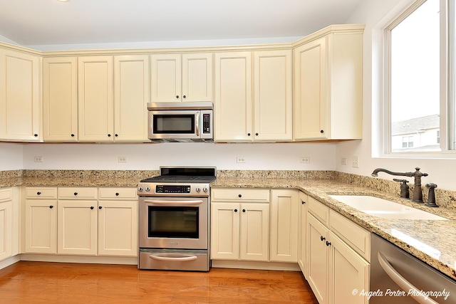 kitchen with stainless steel appliances, cream cabinets, light wood-type flooring, and a sink