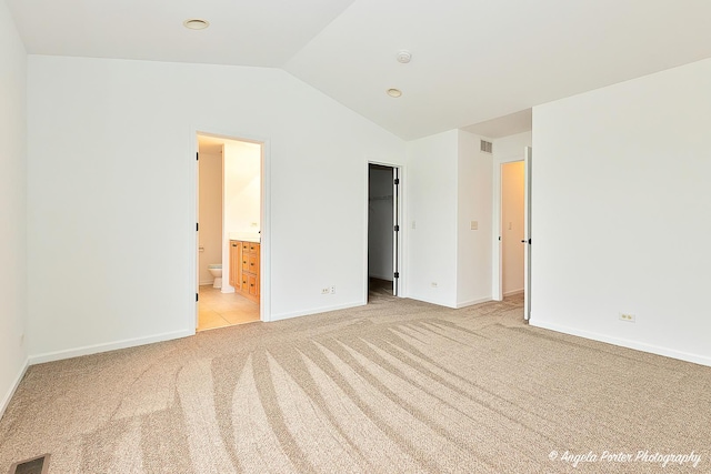 unfurnished bedroom with baseboards, visible vents, light colored carpet, lofted ceiling, and a walk in closet