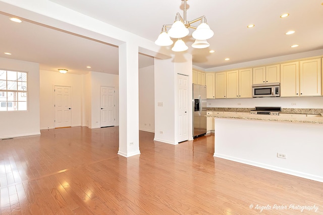 kitchen with light stone counters, stainless steel appliances, open floor plan, cream cabinetry, and light wood-type flooring