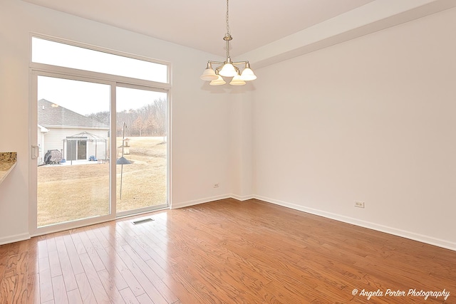 unfurnished room featuring a chandelier, wood finished floors, visible vents, and baseboards