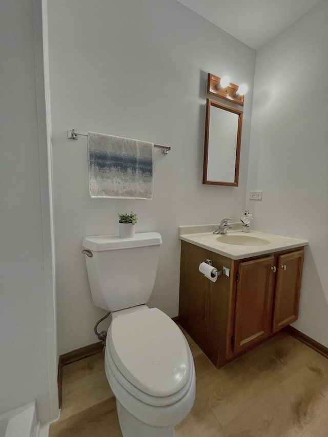 half bath with toilet, baseboards, and vanity