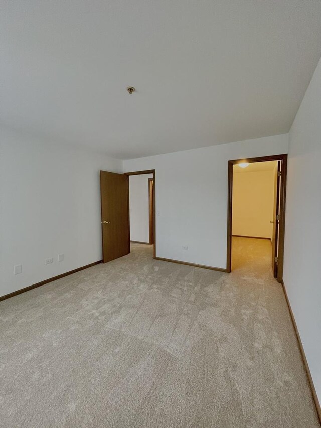 spare room featuring light colored carpet and baseboards