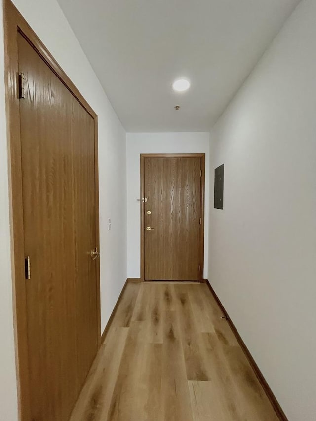 hall with light wood-style floors, electric panel, and baseboards