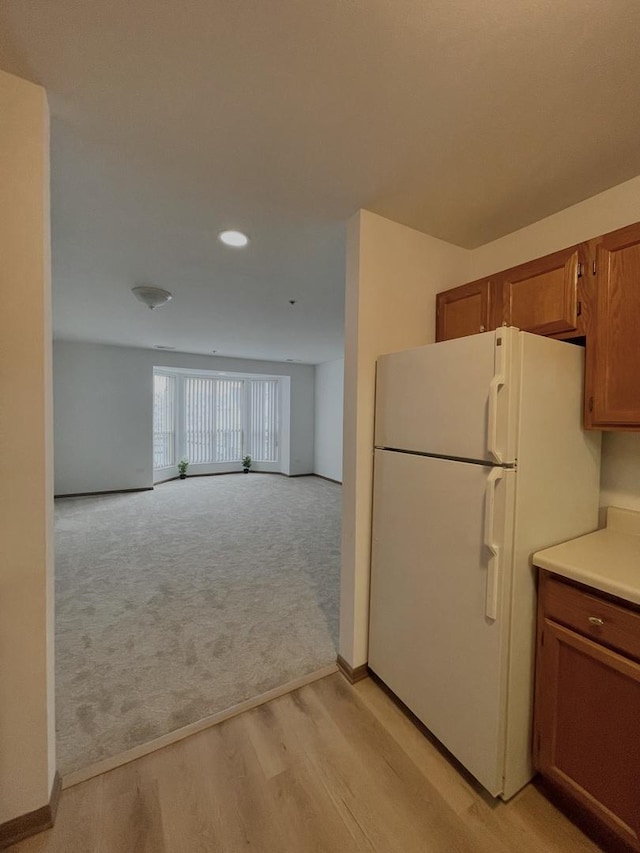 kitchen featuring light carpet, brown cabinetry, freestanding refrigerator, light countertops, and light wood-style floors