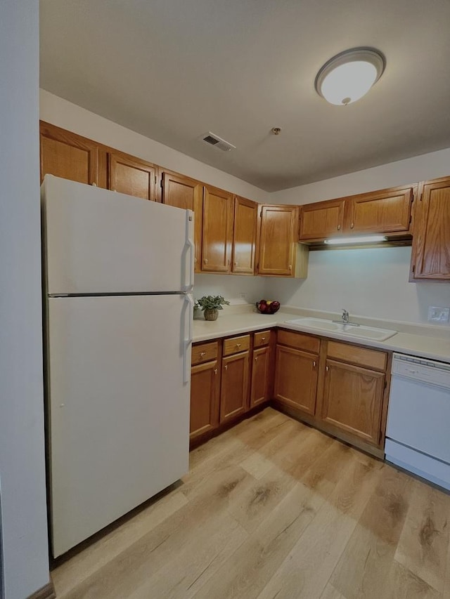 kitchen with white appliances, brown cabinetry, light countertops, light wood-style floors, and a sink