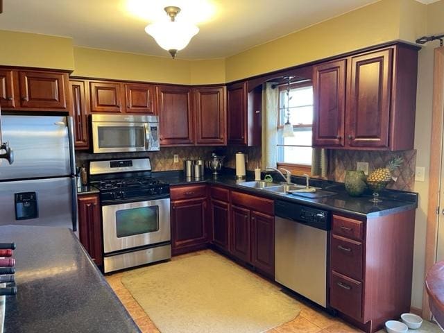 kitchen featuring appliances with stainless steel finishes, backsplash, dark countertops, and a sink