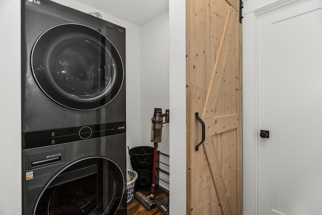 washroom with laundry area, a barn door, and stacked washer / dryer