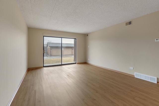 spare room featuring light wood-type flooring, baseboards, visible vents, and a textured ceiling