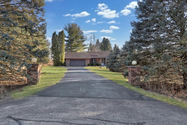 view of front of home featuring aphalt driveway, a front lawn, brick siding, and a garage