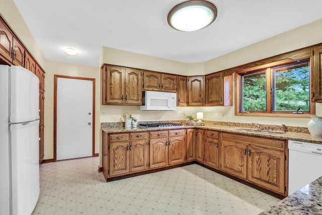 kitchen with light floors, white appliances, a sink, and brown cabinets