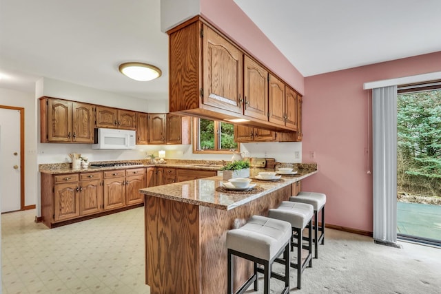 kitchen with baseboards, white microwave, a breakfast bar area, brown cabinets, and a peninsula