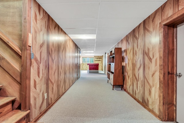 hall with carpet, wooden walls, stairway, and a drop ceiling