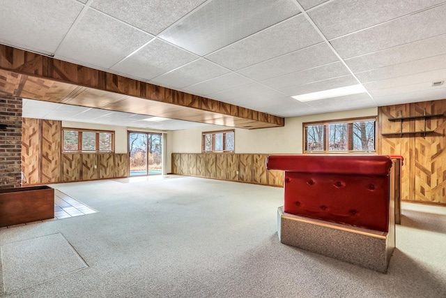 basement with carpet floors, a wainscoted wall, wooden walls, and a drop ceiling