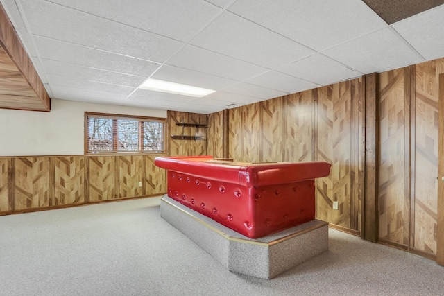 interior space featuring carpet, a paneled ceiling, and wooden walls