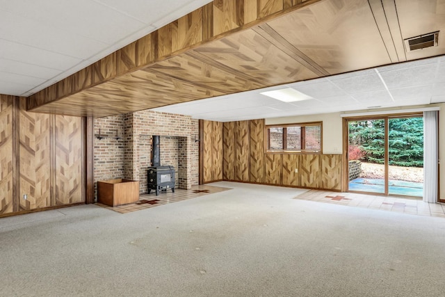 unfurnished living room featuring a wood stove, wooden walls, visible vents, and carpet flooring