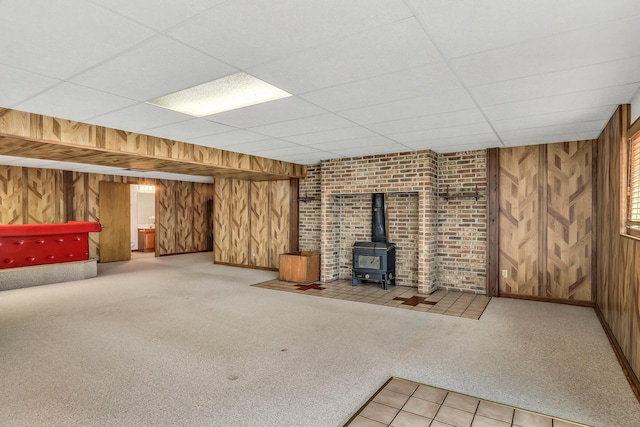 below grade area with carpet floors, a wood stove, a drop ceiling, and wood walls