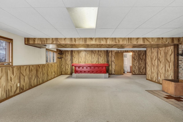 below grade area with carpet flooring, wood walls, and a drop ceiling