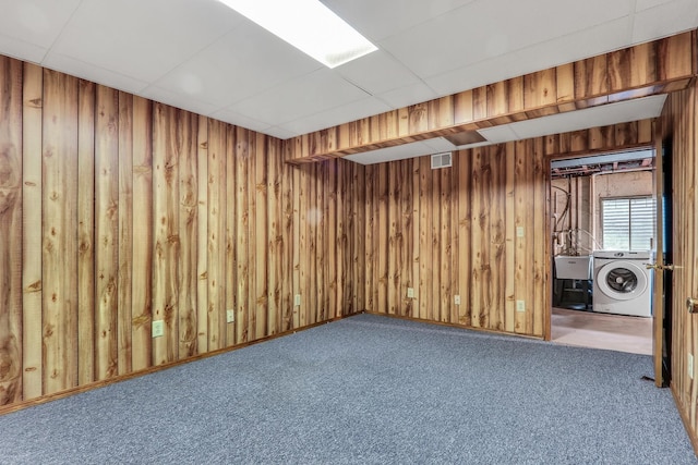 carpeted empty room featuring washer / dryer, a drop ceiling, a sink, and wood walls