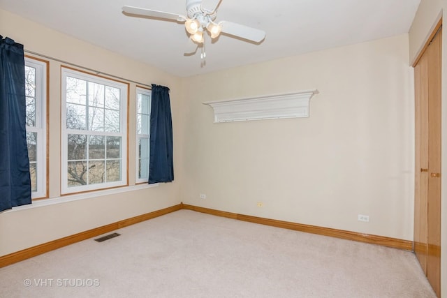 unfurnished room featuring baseboards, visible vents, a ceiling fan, and light colored carpet