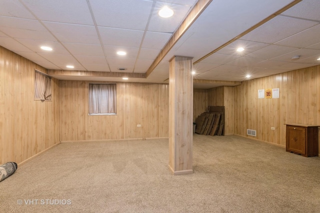 finished basement with carpet floors, visible vents, and wooden walls