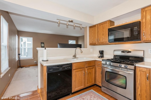 kitchen with a peninsula, a sink, light countertops, brown cabinets, and black appliances