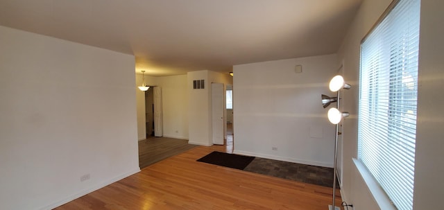 empty room with wood finished floors, visible vents, and baseboards