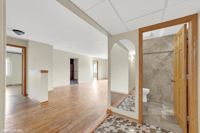 interior space featuring arched walkways, baseboards, a paneled ceiling, and light wood-style floors