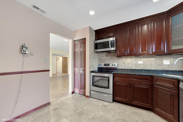 kitchen featuring visible vents, glass insert cabinets, decorative backsplash, appliances with stainless steel finishes, and a sink