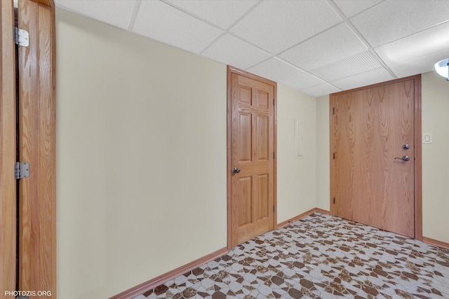 interior space with tile patterned floors, a paneled ceiling, and baseboards